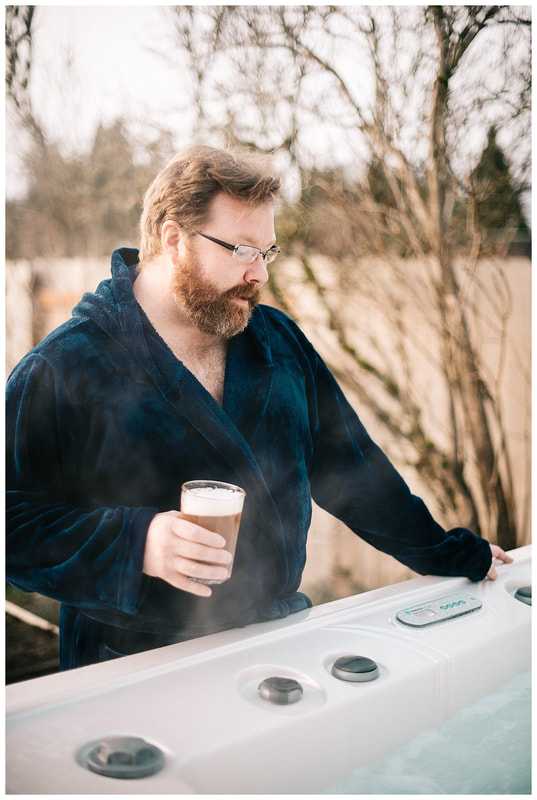 Man with beard in robe standing by hot tub drinking beer for dudeoir photoshoot.